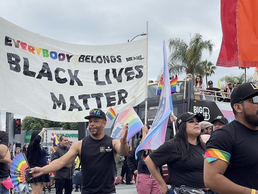 2023 LA Pride Parade in Hollywood marcher with rainbow fan in front of Black Lives Matter banner