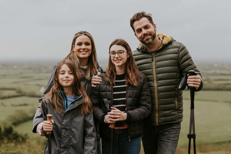 A family photo of a man, woman, and their two middle grade aged children standing together at the end of a hike.