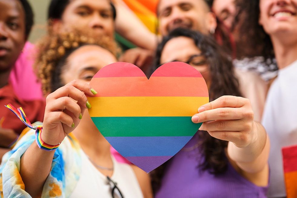 A group of LGBTQ people holding a rainbow heart celebrating International Pride Month.