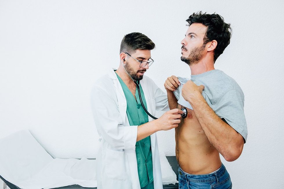 A male doctor performs a check-up on a male patient in his 30s. He use a stethoscope to monitor heart and lung function during a medical consultation in public healthcare facilities. White background