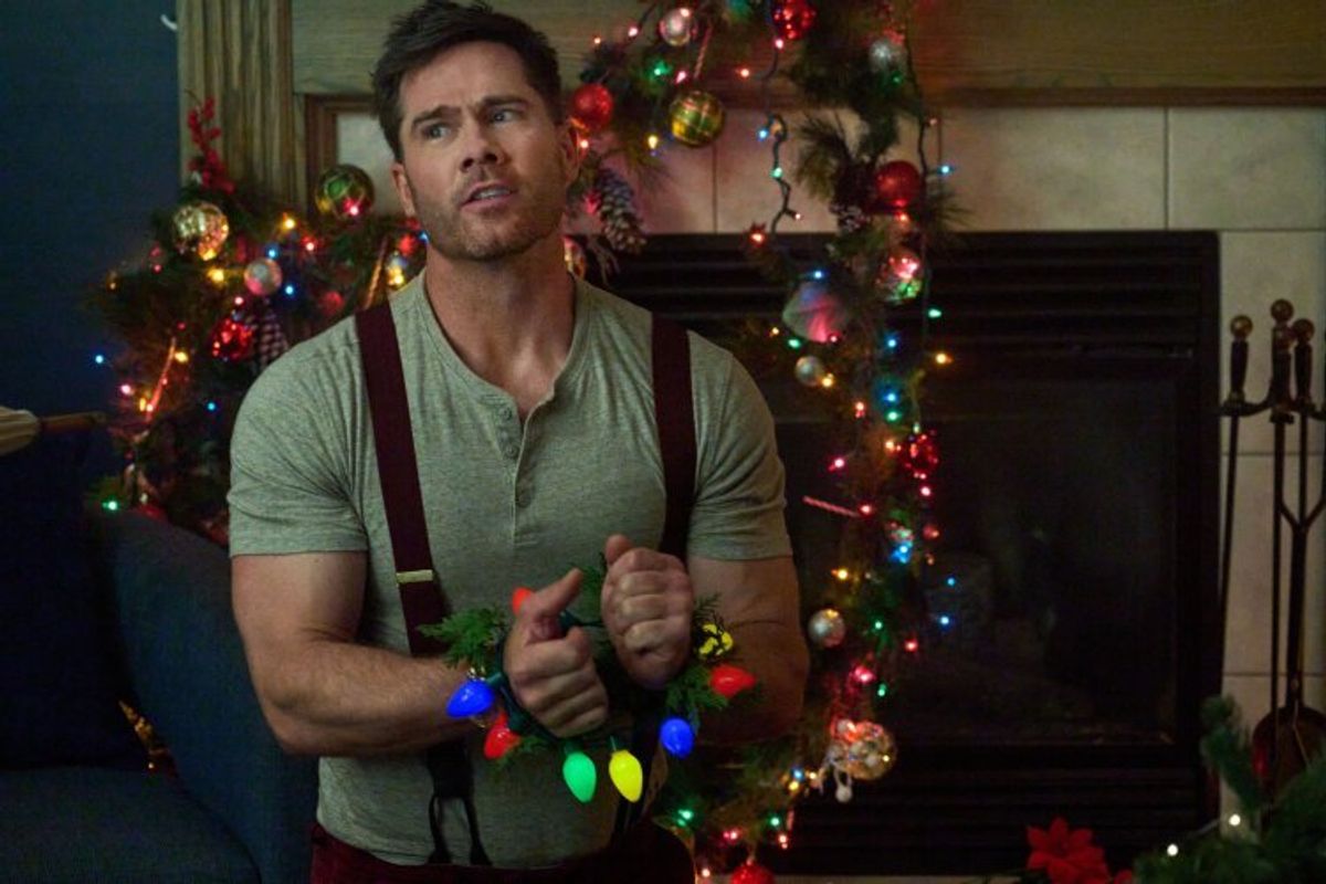 A man on his knees with his wrists tied up with Christmas lights.