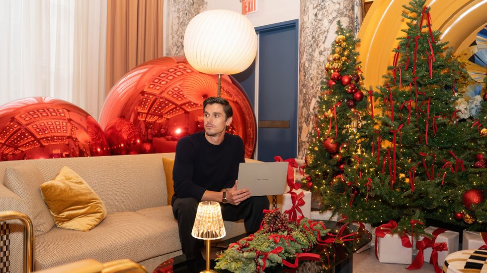 A man sitting on a couch with a laptop next to Christmas trees