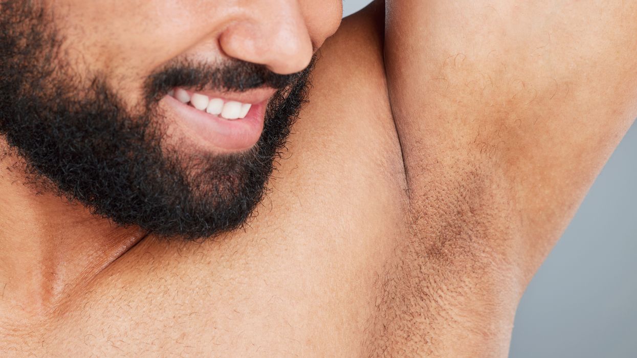 A man smiling while sniffing his armpit