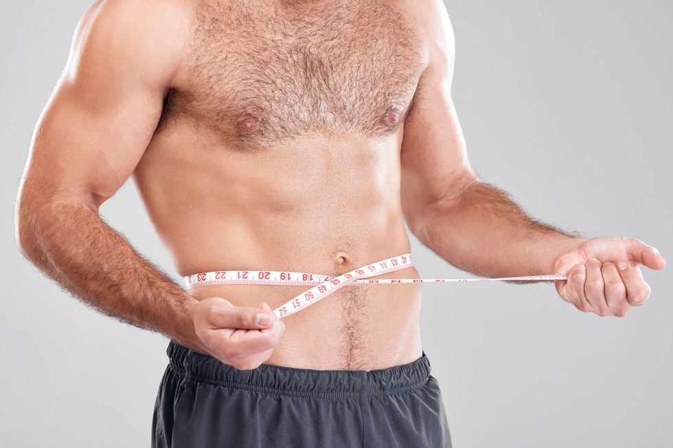 A shirtless man holding a tape measure around his waist.