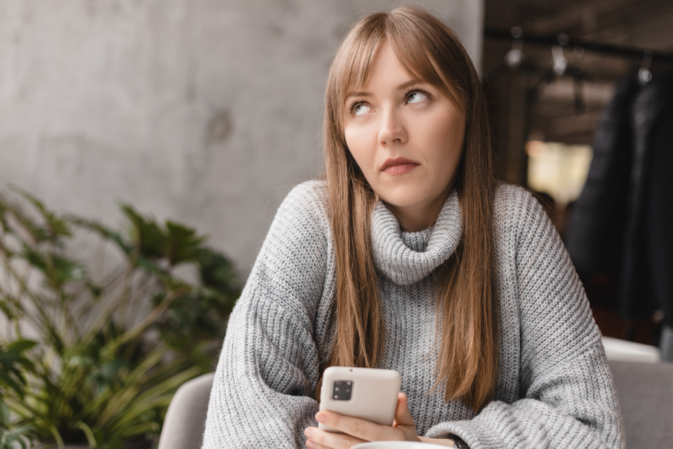 A woman sits with her phone in her hand, rolling her eyes.