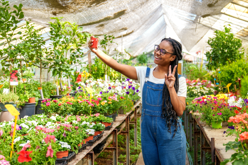 A woman taking a selfie surrounded by flowers at a greenhouse.