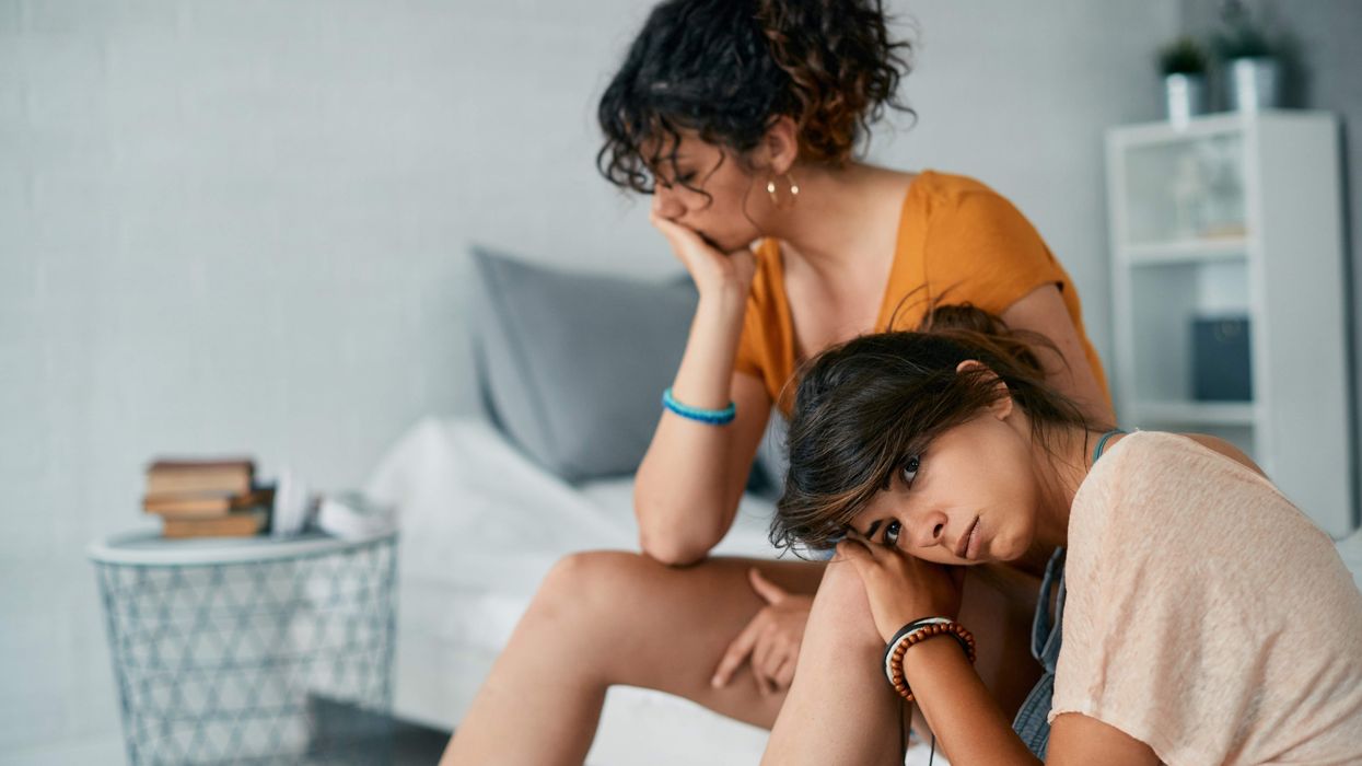 A women sitting with her face turned away while another woman leans her head on her knee and looks at the camera