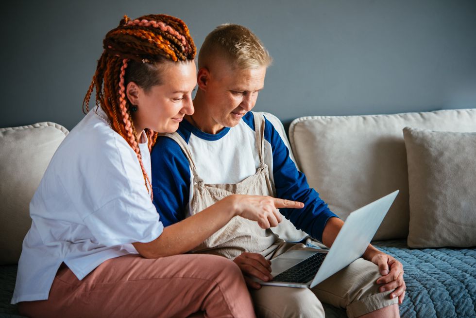 Beautiful lesbian couple cuddling on the couch watching movie on laptop or shopping. LGBTQ relationship and lifestyle concept.