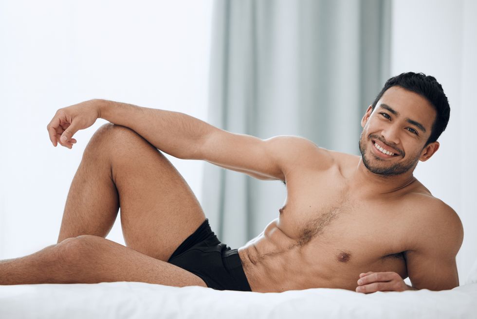 Body, relax and portrait of Asian man on bed with pride, smile and wellness on weekend in home. Male person, abs and topless with face, strength and confident in morning or wakeup in apartment