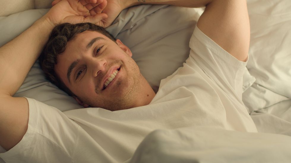 Caucasian happy man sleeping open eyes wake up looking at camera smiling good morning comfortable cozy guy rest relaxation bedroom bed hotel wellbeing positive weekend male pleasure home satisfaction