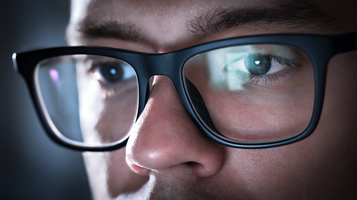Close up of man with a reflection of a computer screen in his glasses.