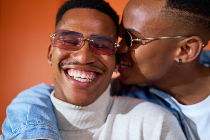 Close up portrait happy, carefree young gay male couple in sunglasses laughing and biting ear playfully