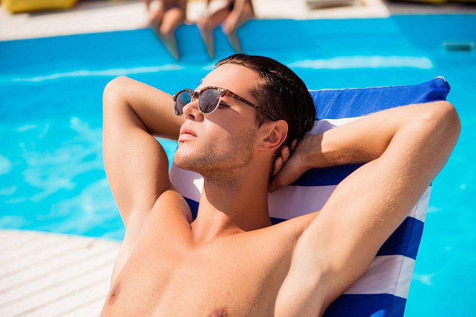 Close up portrait of serene young handsome brunet mature guy in tredy sun glasses, tanning near the pool with arms behind the head, with closed eyes