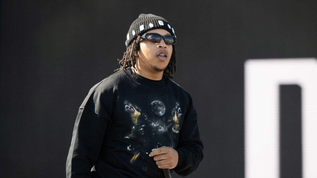DDG in a black sweater and beanie holds a microphone on stage.