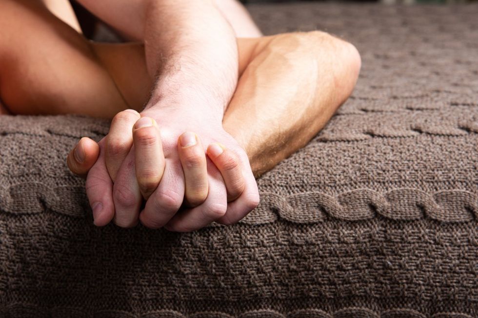 Gay men hold hands in bed.