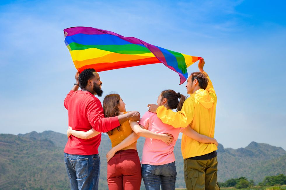 group of diverse lgbtq friends wearing colorful clothes, standing side by side, smiling and holding lgbt flags waving in the air, concept of lgbt community equality movement, lgbt happy pride month