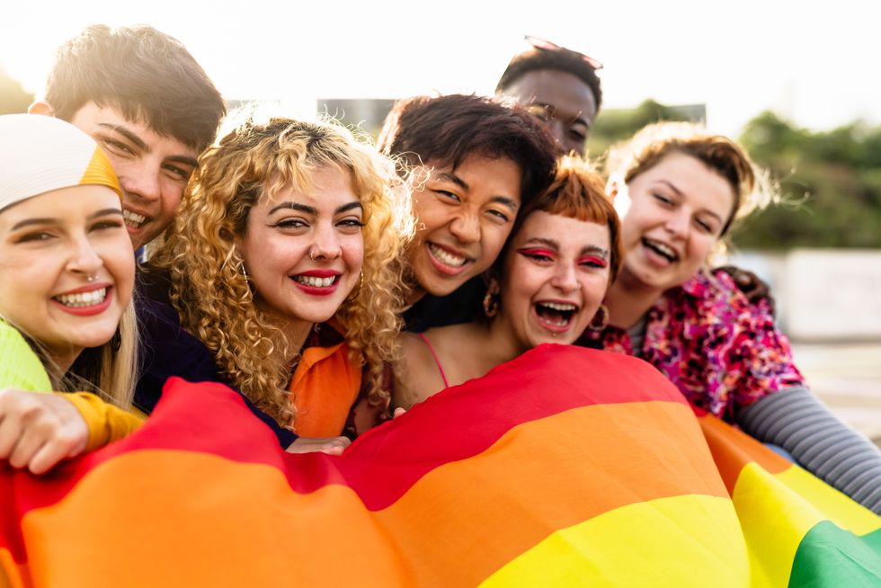 group of queer people laughing behind a flag