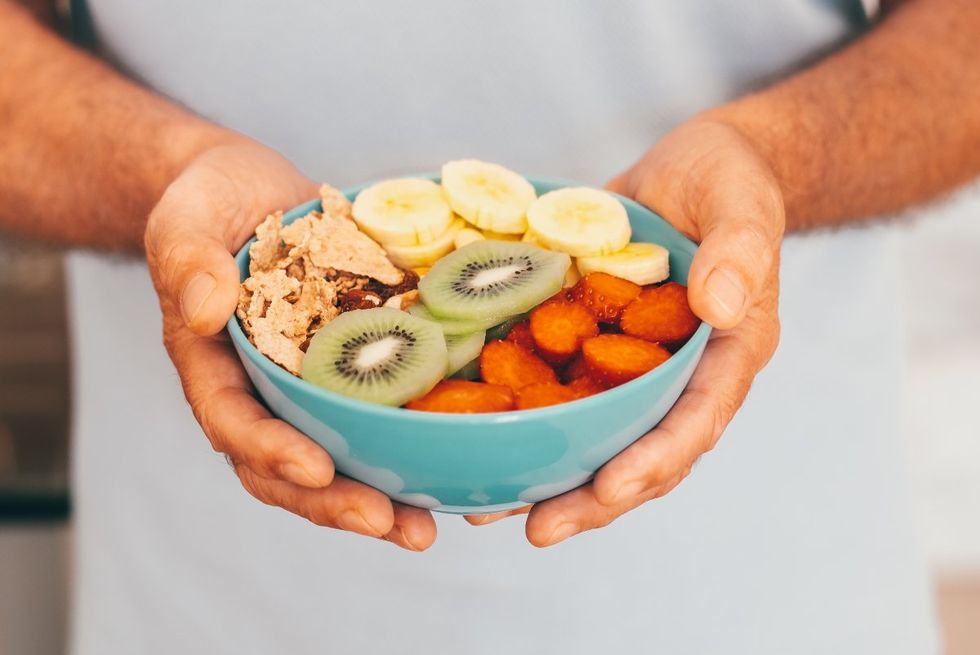 Hands holding a ready to eat fruit salad with kiwi banana strawberries and dried fruits.