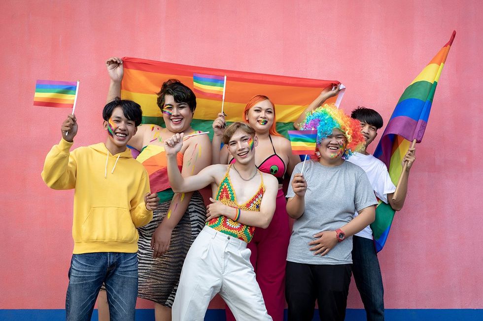 Happy Asian young friends holding rainbow flag celebrating gay pride festival - LGBTQ community concept