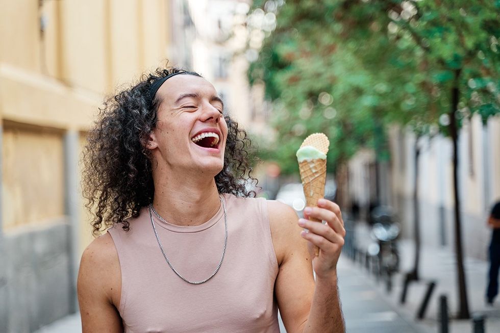happy gay man walking down the street with an ice cream cone in his hand laughing loudly