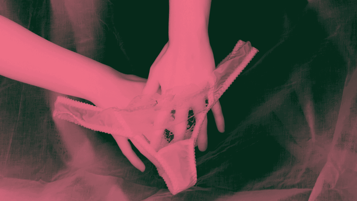 Lace panties being held by two hands against a dark background.