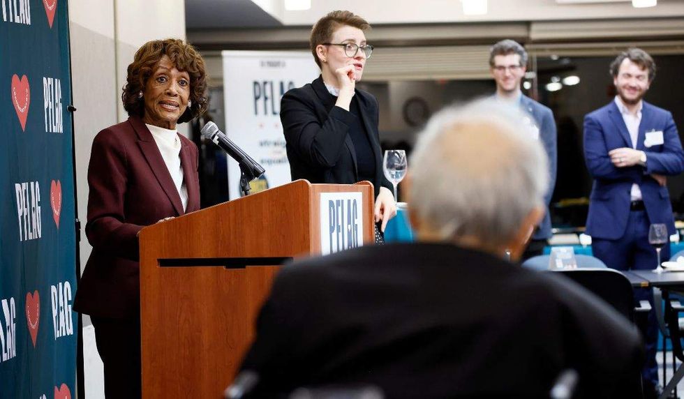 Maxine Waters speaking at a podium with former Rep. Barney Frank listening.