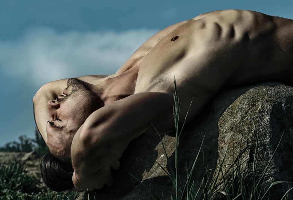 naked man posing over a rock