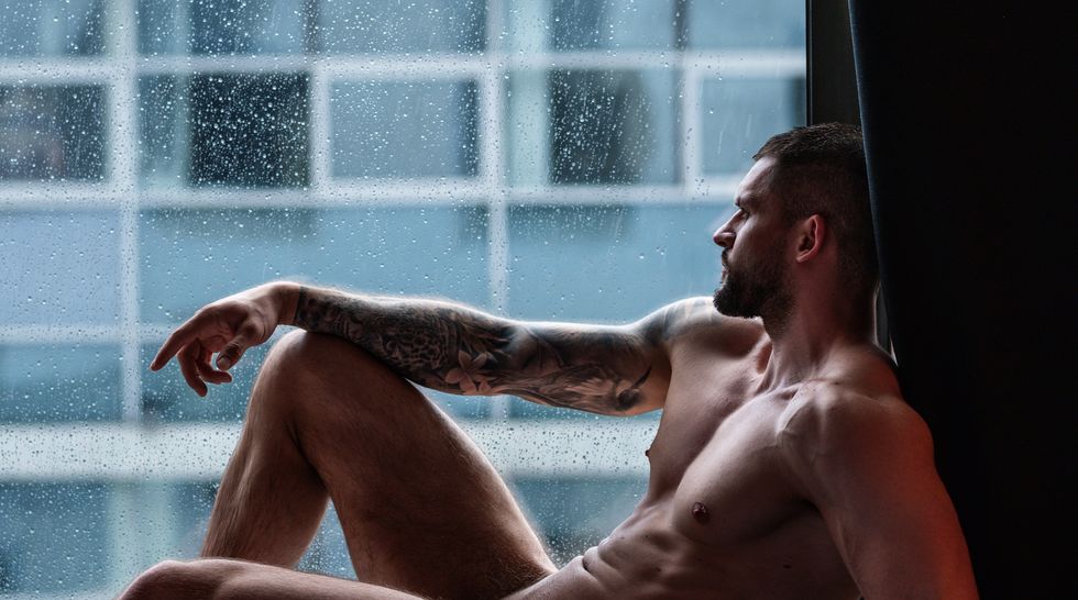 naked man staring out a window