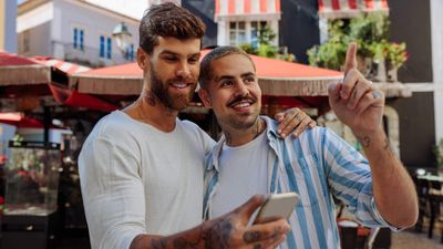 On man looking at his cell phone while a second man points at something in the distance