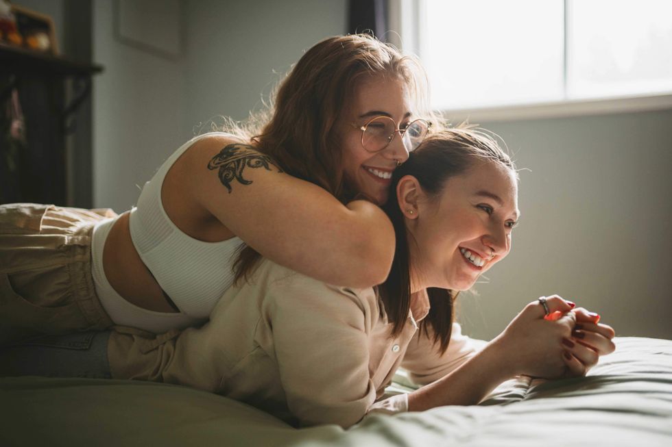 One lesbian lying on top of another in bed