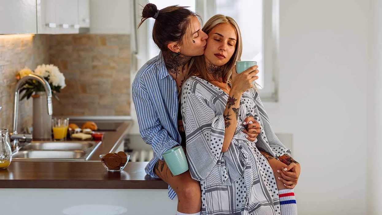 One lesbian sitting on the kitchen counter with another lesbian standing in front of her