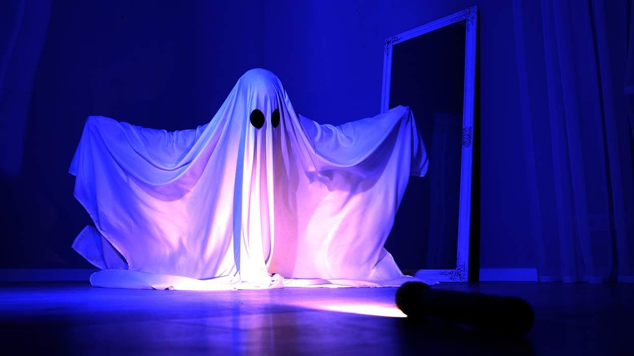 person in ghost costume making spooky pose in dark room into a flashlight