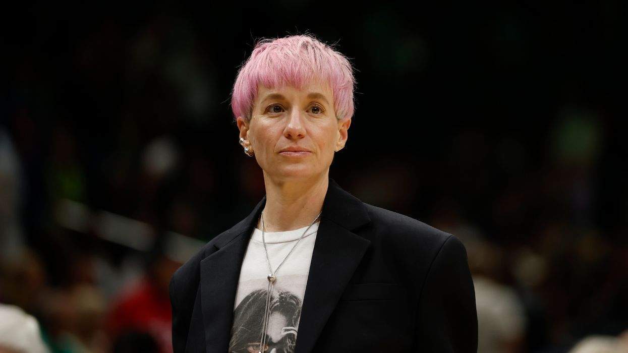 Person with short pink hair wearing a blazer and graphic t-shirt, looking ahead.