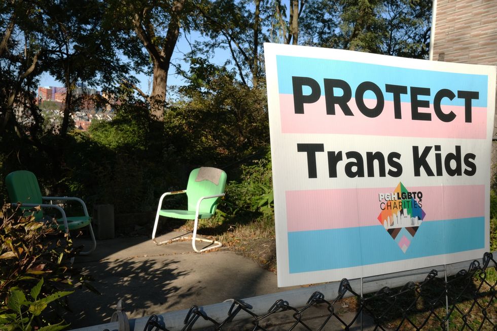 Pittsburgh, PA USA. October 13,2022. Protecting trans kids sign seen near an old green vintage yard chair on a sunny day in the Polish Hill neighborhood of Pittsburgh Pennsylvania.