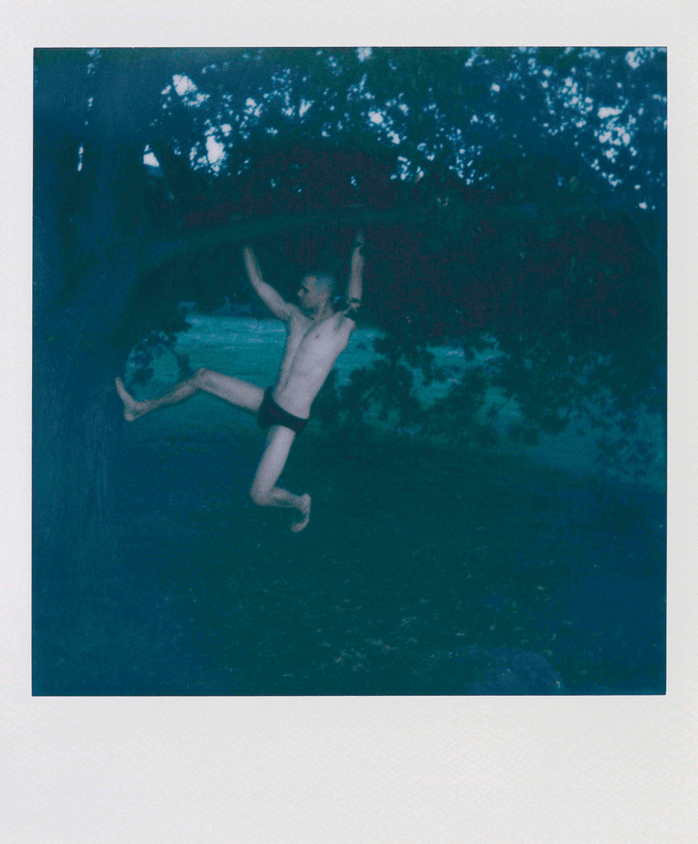 Polaroid image of a man swinging from a tree trunk.