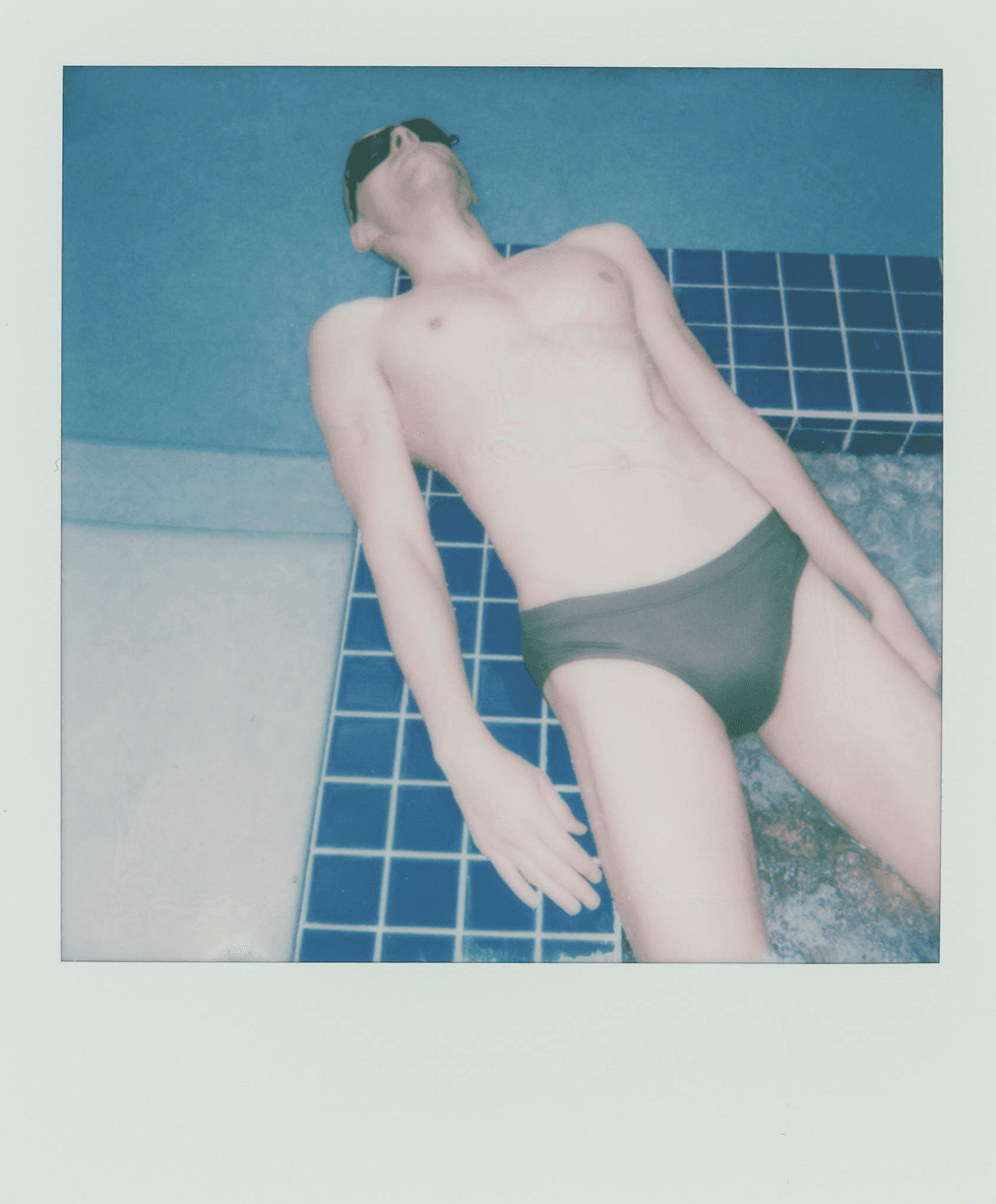 Polaroid portrait of a man floating in a pool wearing dark briefs.
