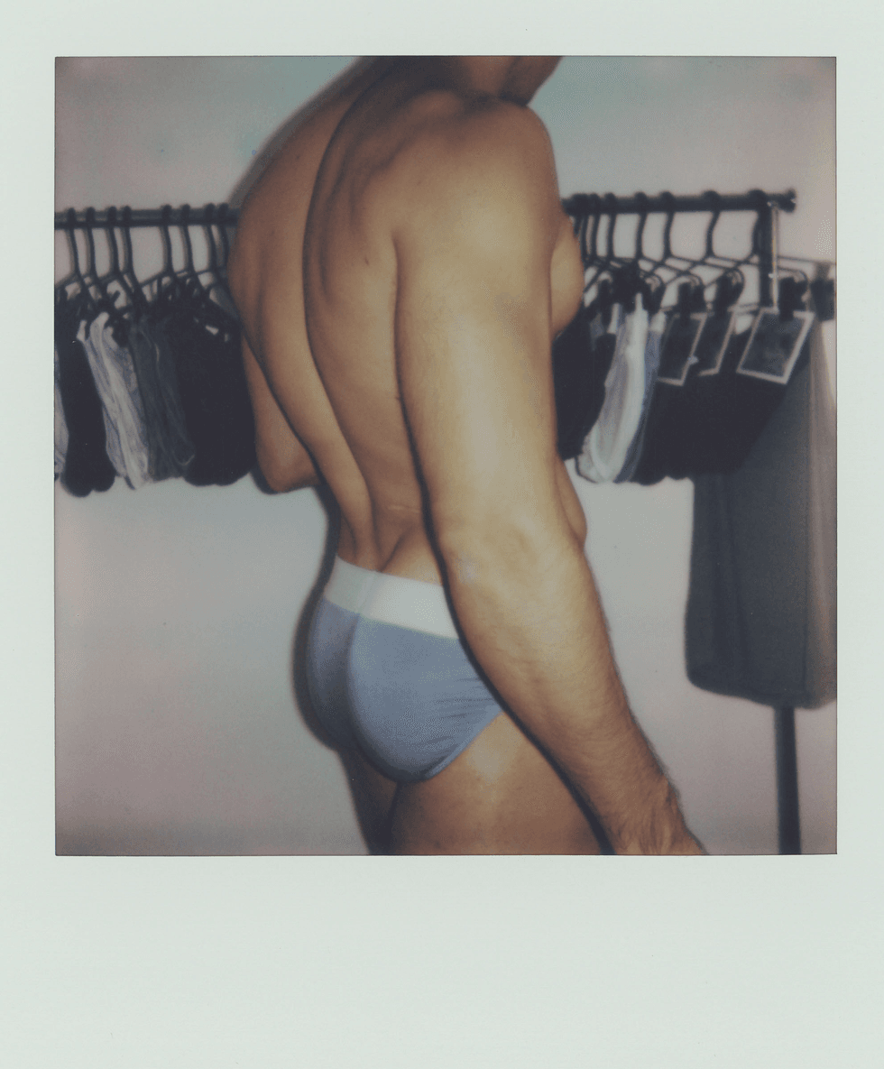 Polaroid portrait of a man from behind wearing briefs beside a clothing rack.