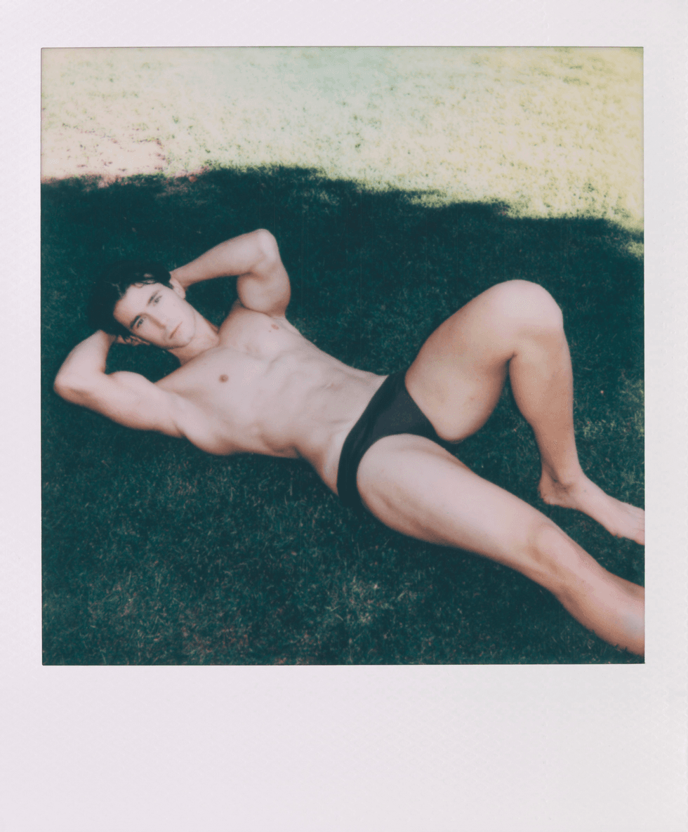 Polaroid portrait of a man reclining on grass wearing dark briefs.
