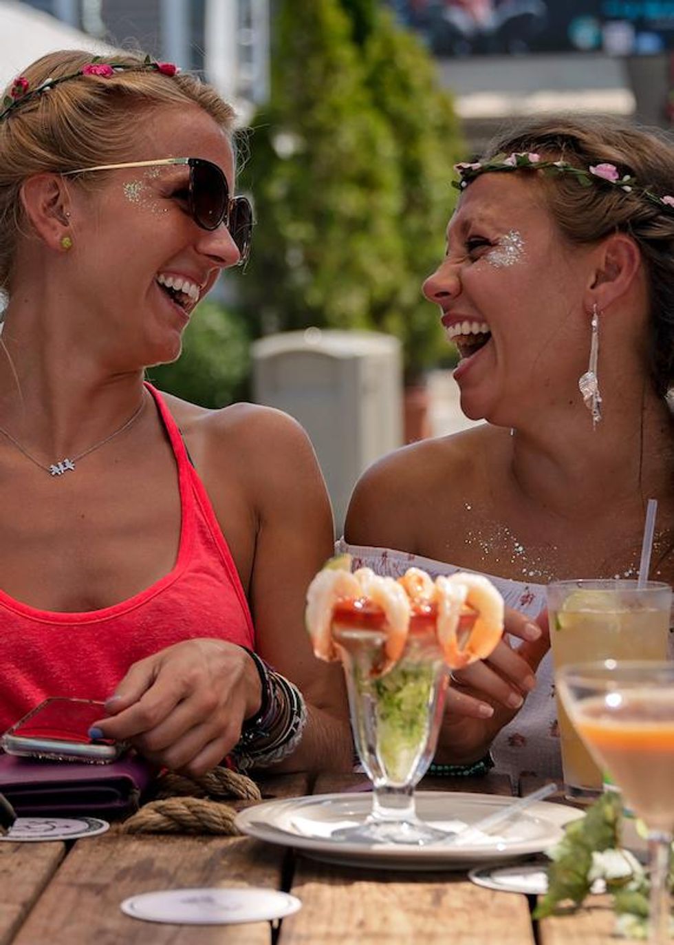 Queer couple laughing over shrimp cocktails on an outdoor dining patio