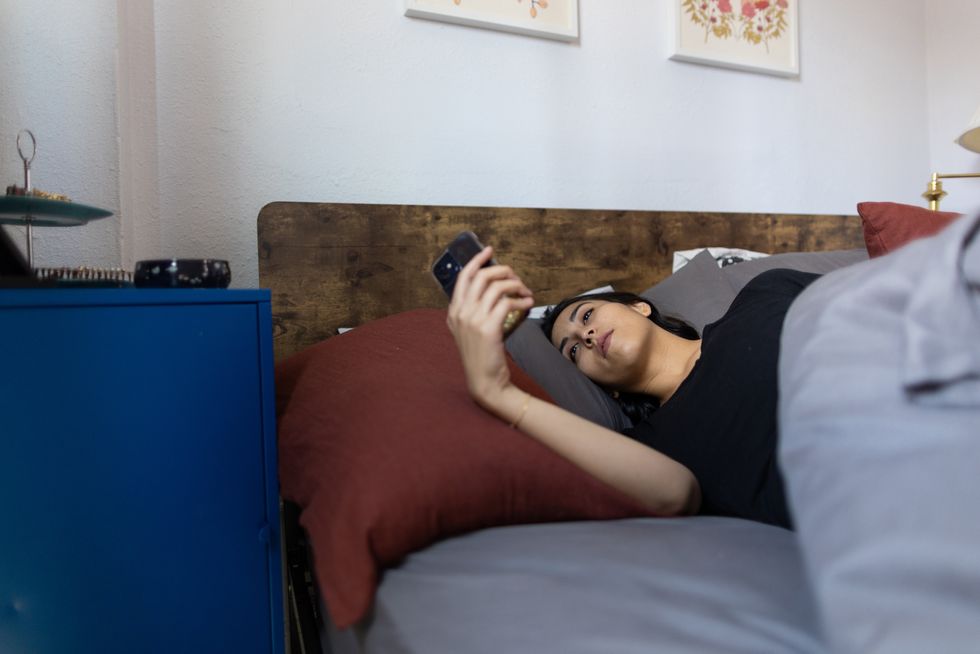 queer person looking at phone in bed