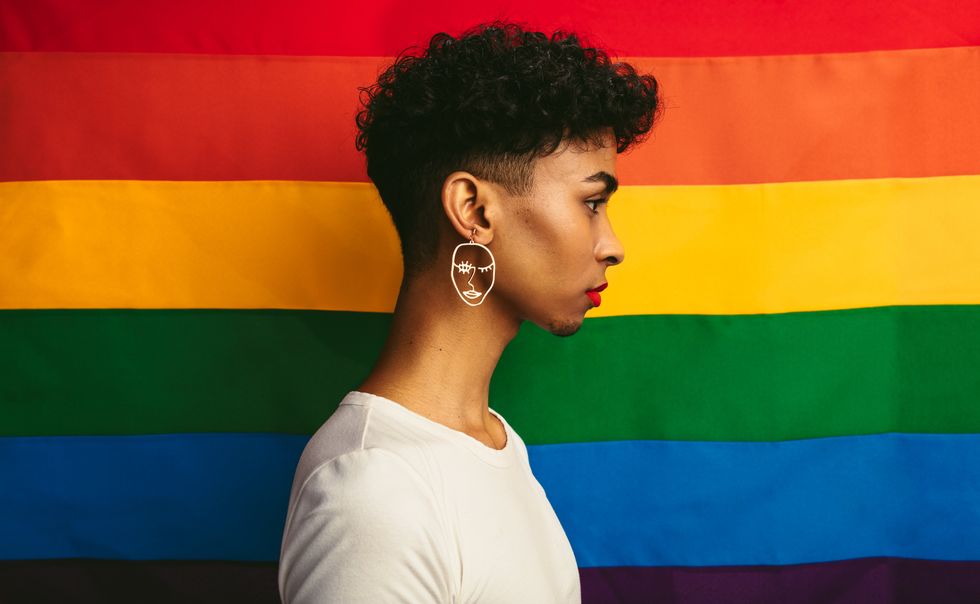 queer person posing in front of a pride flag