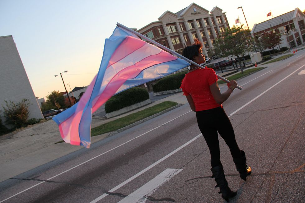 Raquel walking in a pride parade while holding a trans flag.
