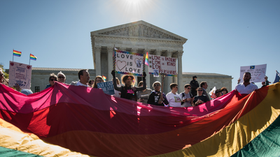 Same-sex marriage demonstrators hold up Love is love signs and a huge rainbow flag in front of the Supreme Court