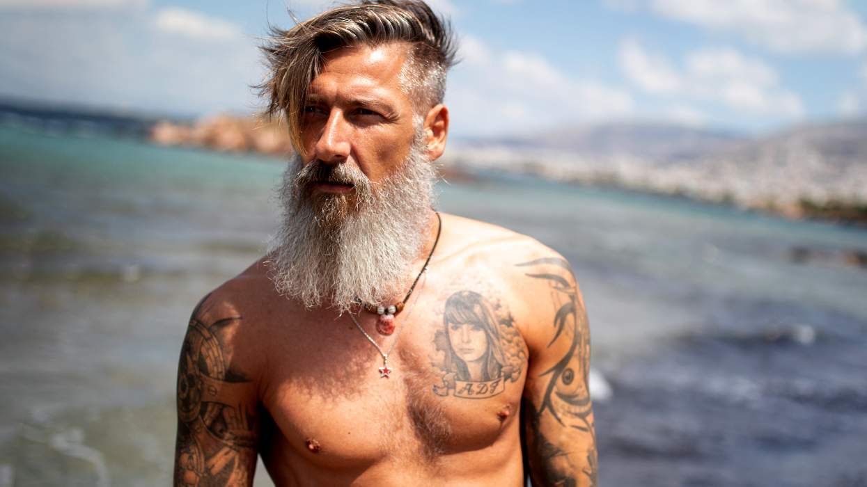sexy slim muscular silver bearded man with tottoos at the ocean