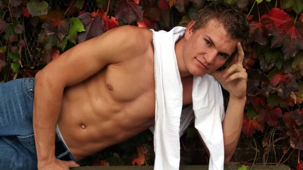 Shirtless man in front of fall leaves