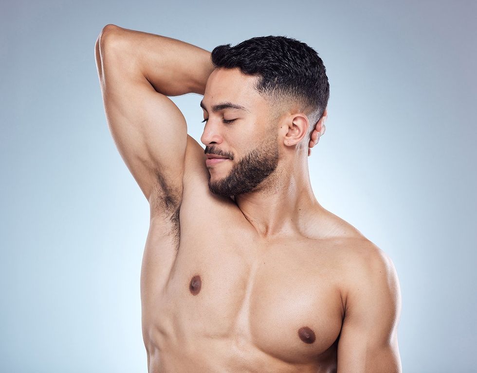 Smile, man and smelling armpit for hygiene with skin health and deodorant fragrance for self care in studio. Happy male person, underarm and check sweat for clean body and perfume by gray background