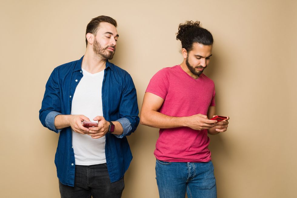 Suspicious jealous gay man spying on his boyfriend texting on his smartphone in front of a yellow background