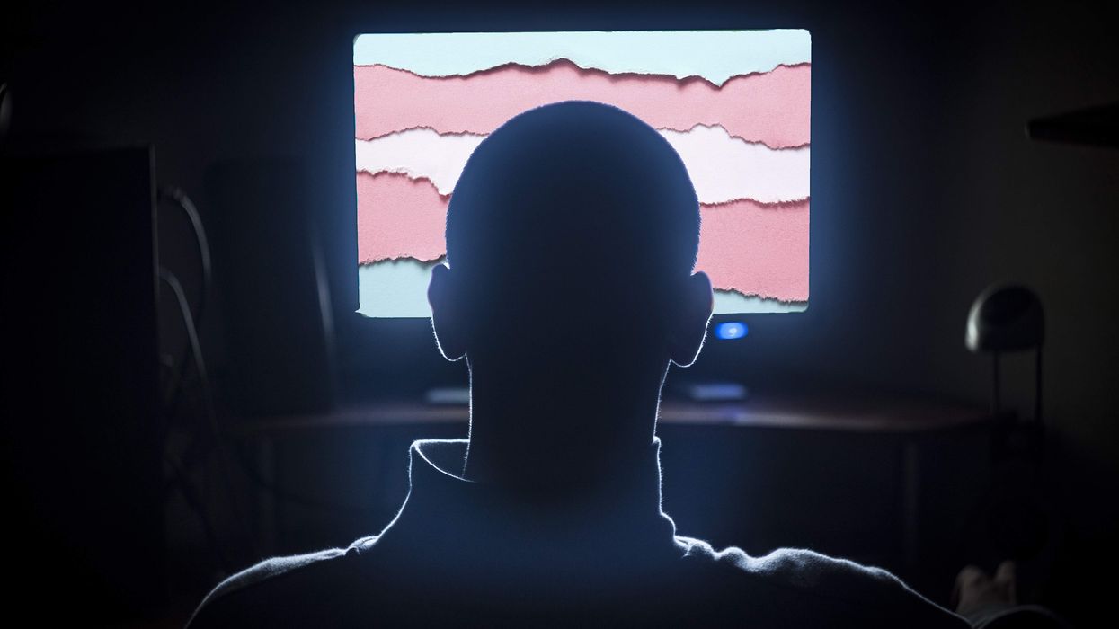 The silhouette of a man in front of a computer screen with the trans flag