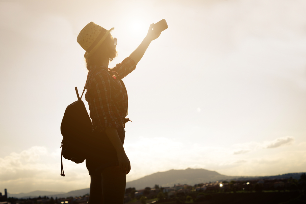 The silhouette of a woman taking a selfie outside.