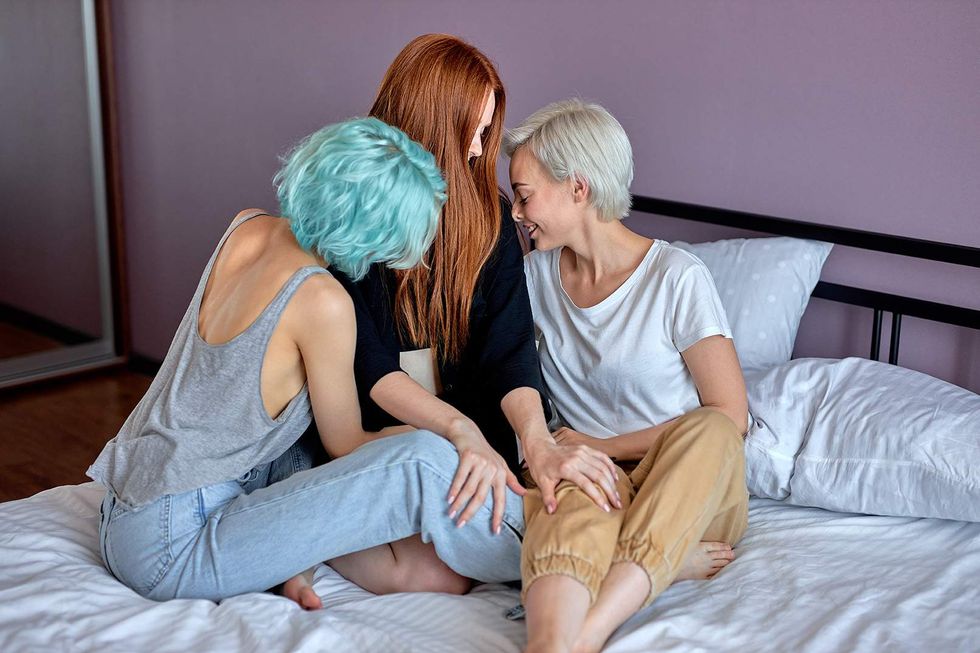 three women sitting on a bed touching each other